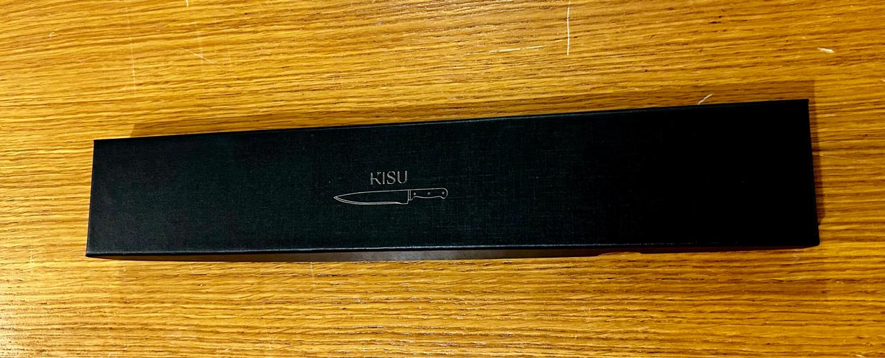 Professional chef knife in sleek black packaging on wooden surface.
